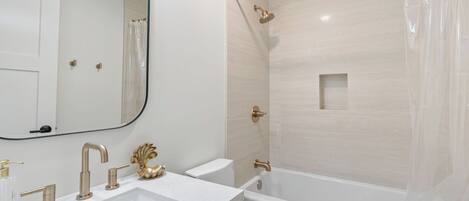 A modern bathroom with a large mirror, a bathtub, a shower with a glass door, and a vanity with a gold faucet.