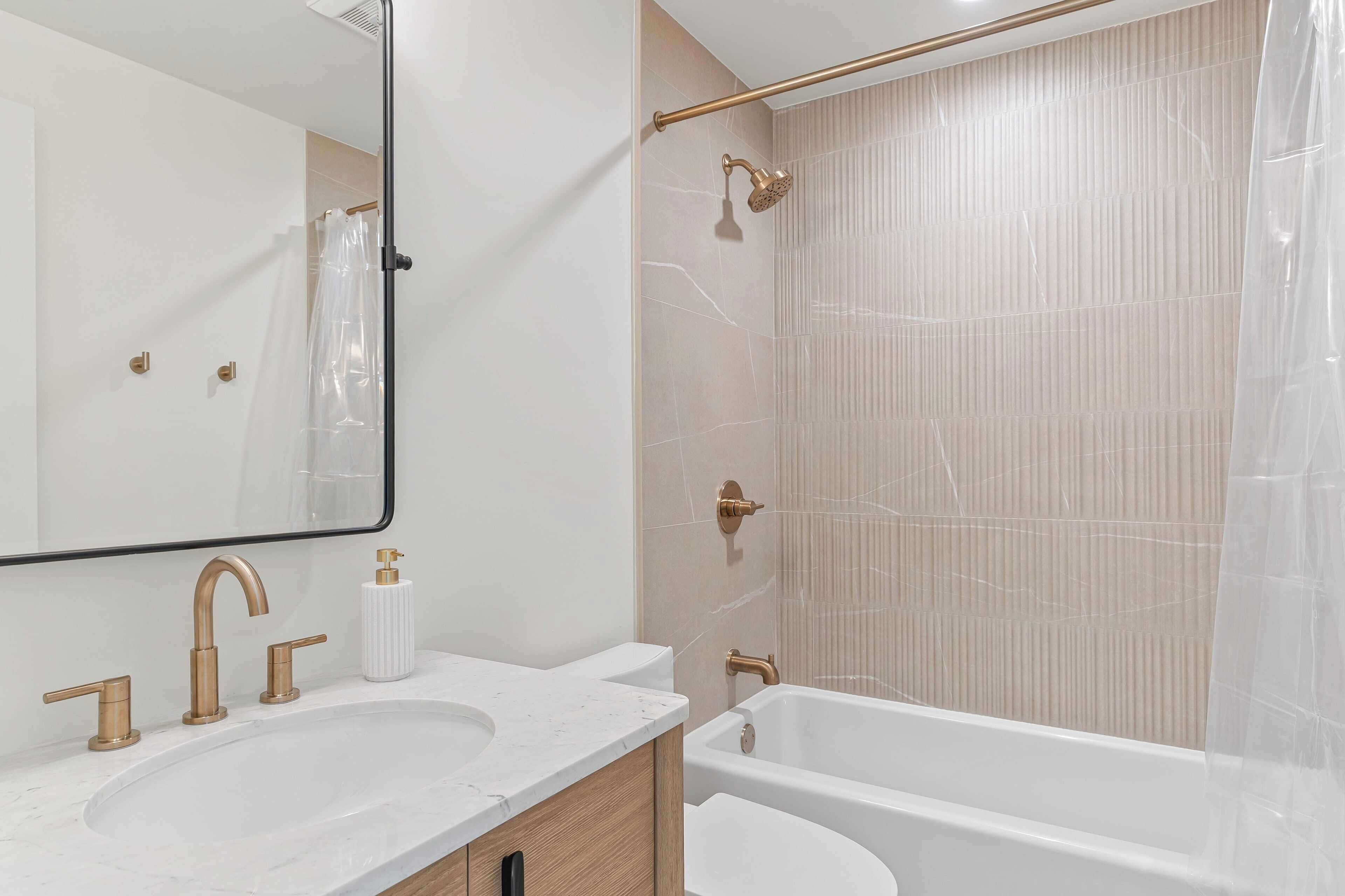 A bathroom with a large mirror, two sinks with gold faucets, a bathtub, and a shower curtain.