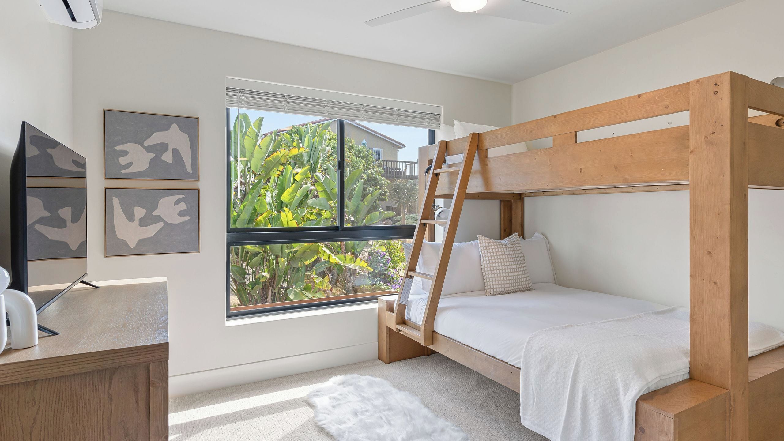Una cama individual superpuesta con escalera, un escritorio con silla, una alfombra blanca y una ventana con persianas.