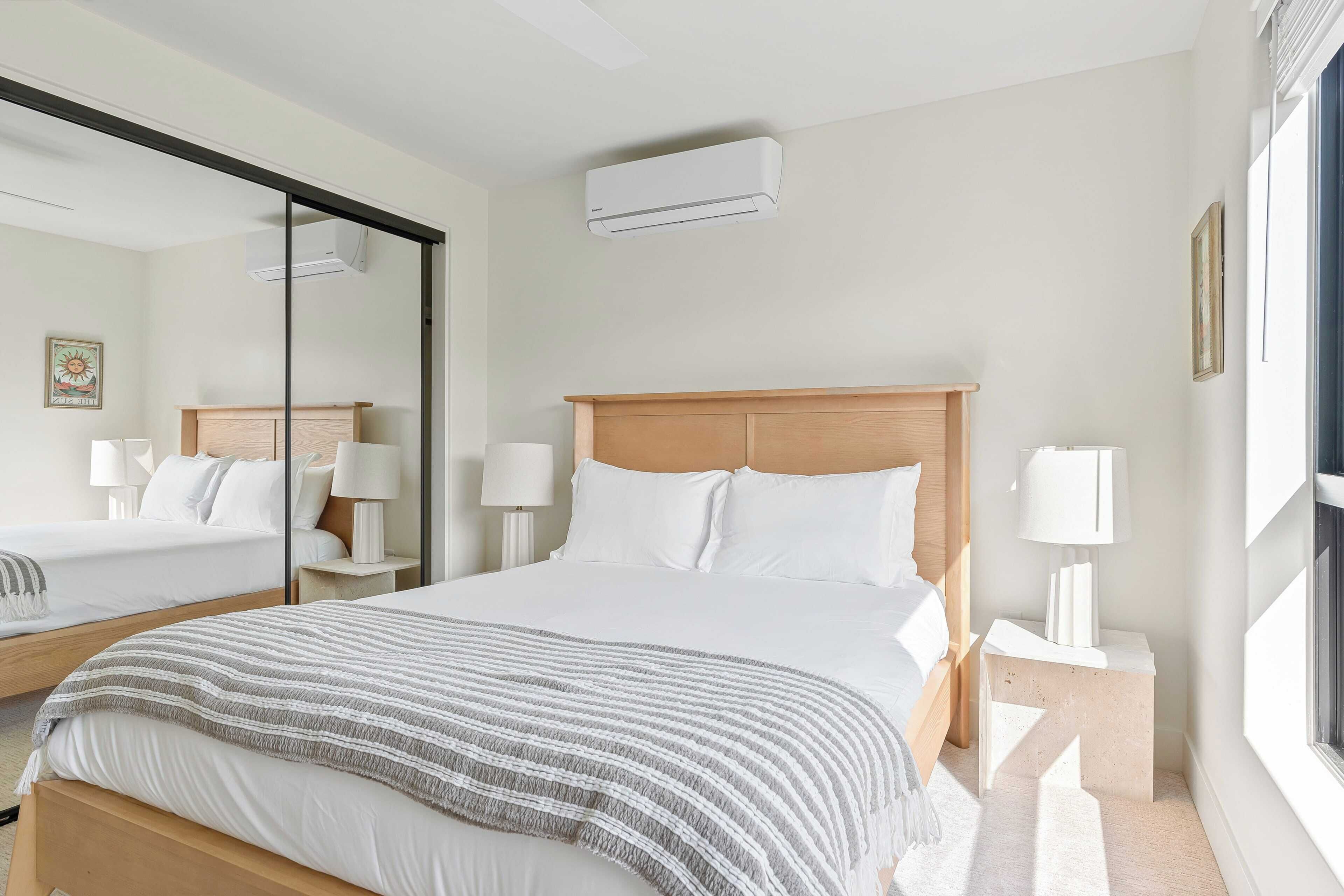Habitación de hotel con una cama grande, una mesita de noche con lámpara, un espejo y un equipo de aire acondicionado.
