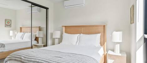 Habitación de hotel con una cama grande, una mesita de noche con lámpara, un espejo y un equipo de aire acondicionado.