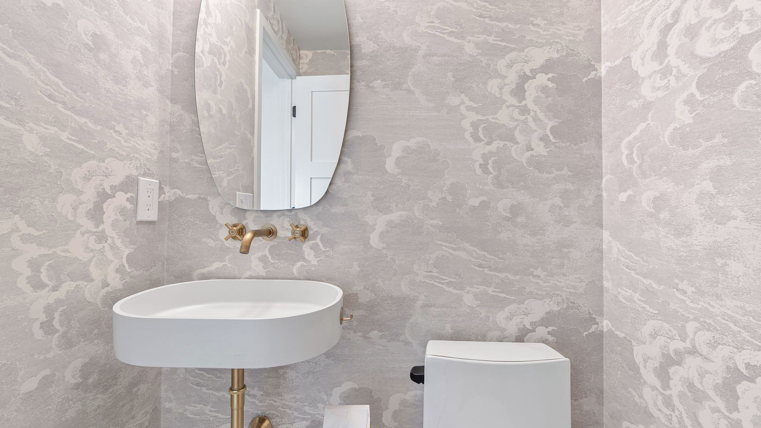 A bathroom with a white sink, gold faucets, a white toilet, and a wall-mounted mirror.