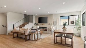 A spacious living room with a fireplace, a wooden staircase, and a large window.