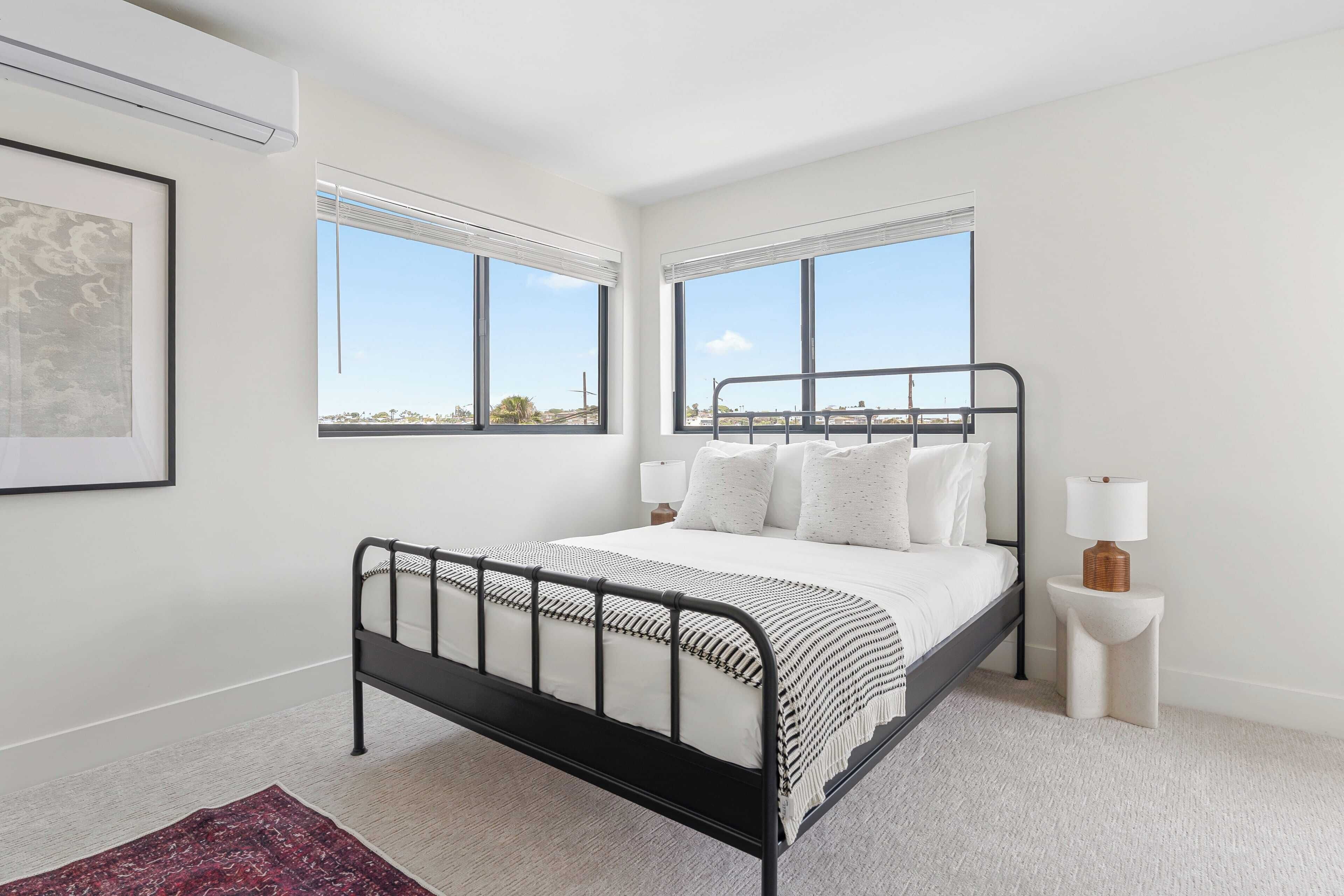 A modern bedroom with a black metal bed frame, white bedding, and two bedside tables with lamps.