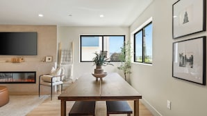 A modern living room with a wooden dining table, a fireplace, and a large window.
