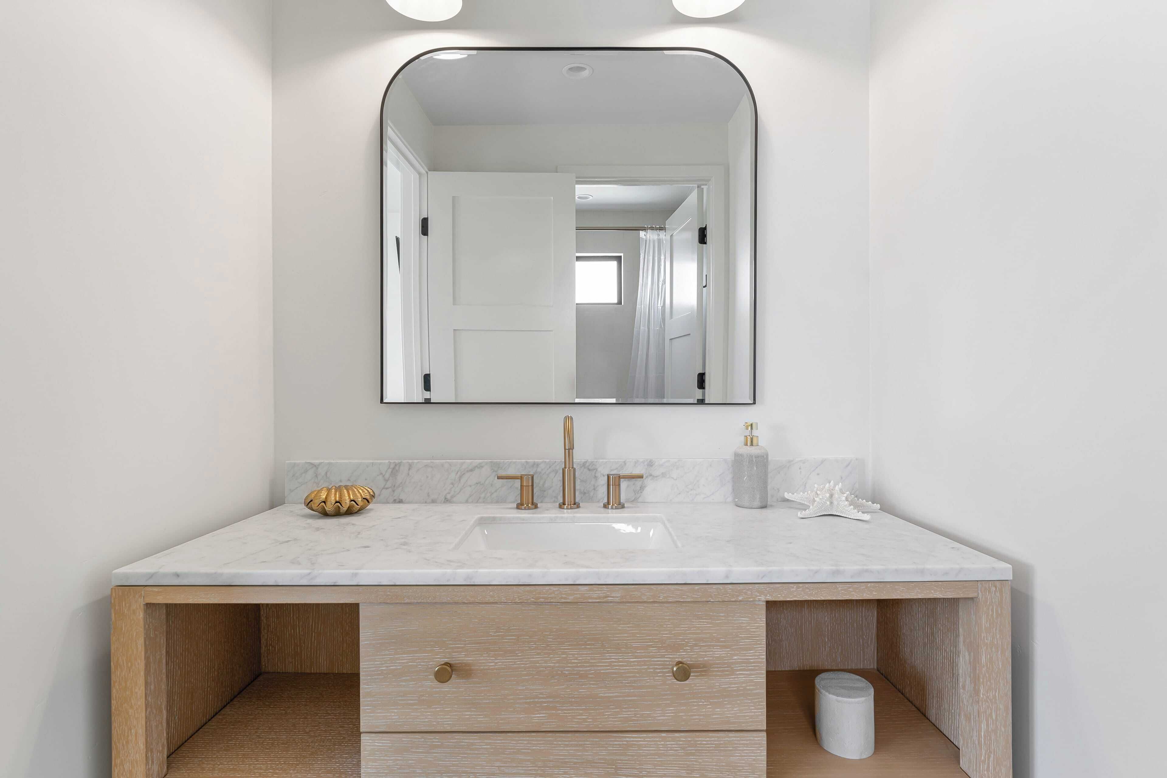 Un bagno con un lavabo in marmo, una cassettiera in legno e uno specchio grande.