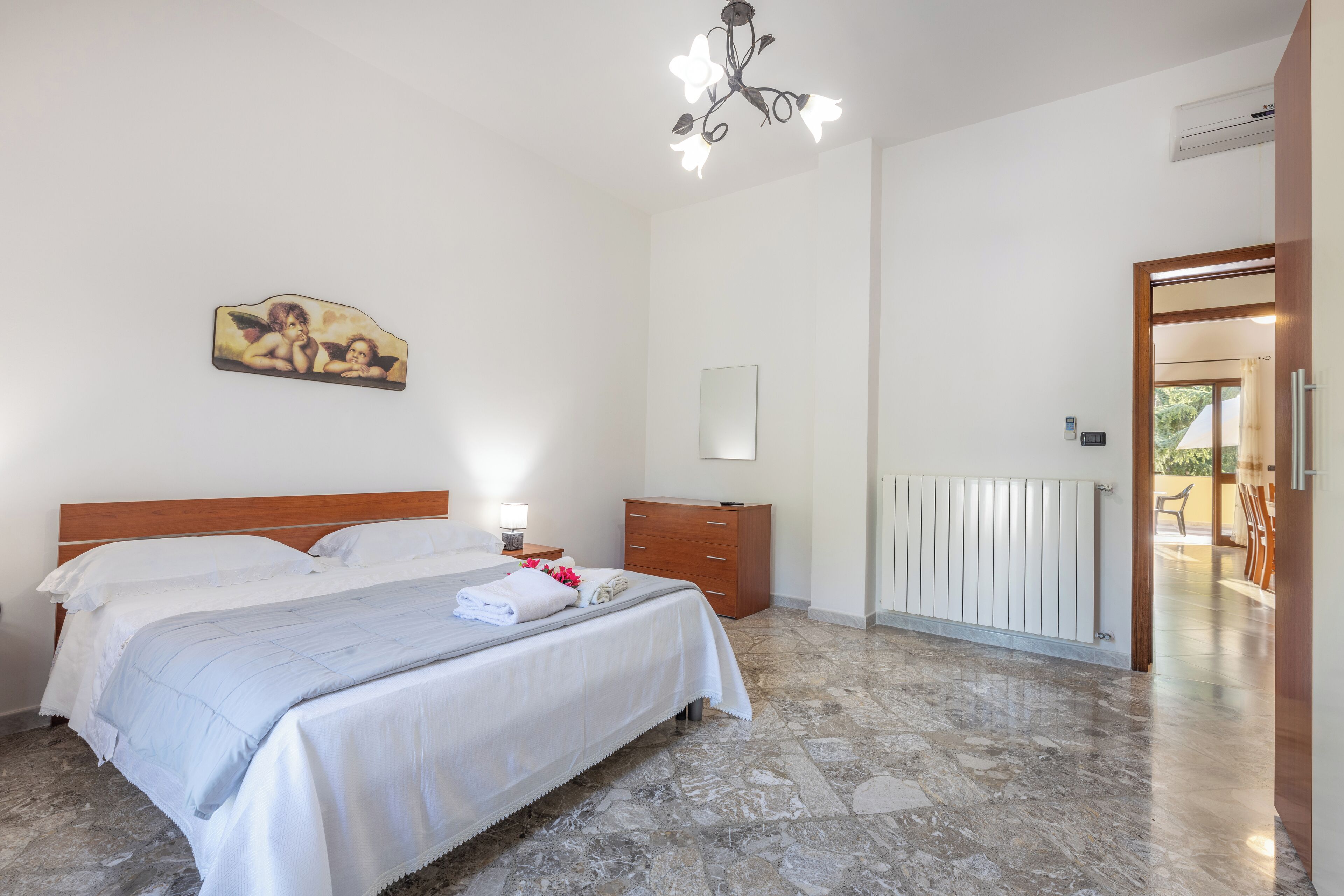 A bedroom with a bed, a nightstand, a dresser, a chandelier, and a radiator.