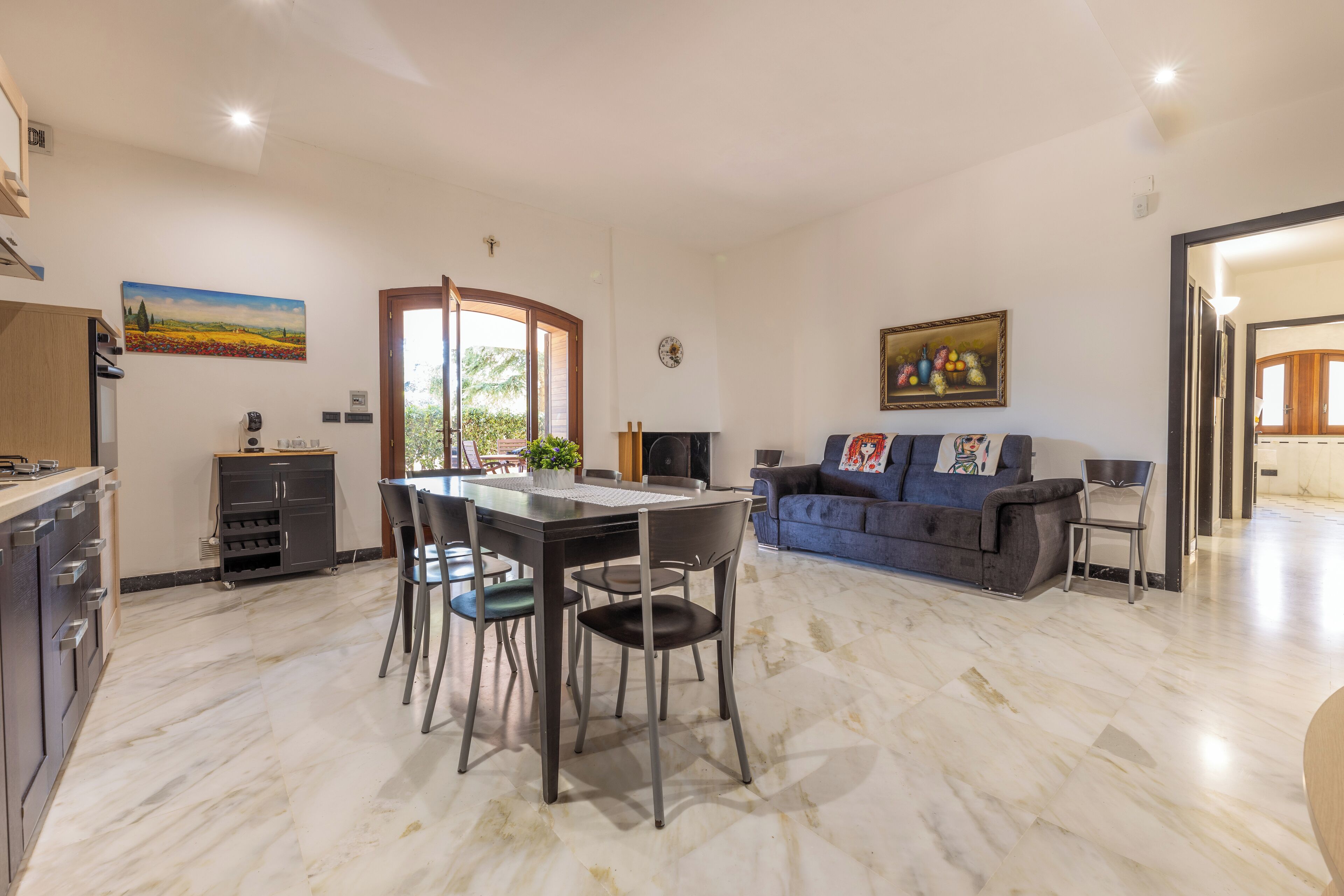 A spacious living area with a dining table, chairs, a sofa, and a kitchen area with cabinets and a countertop.