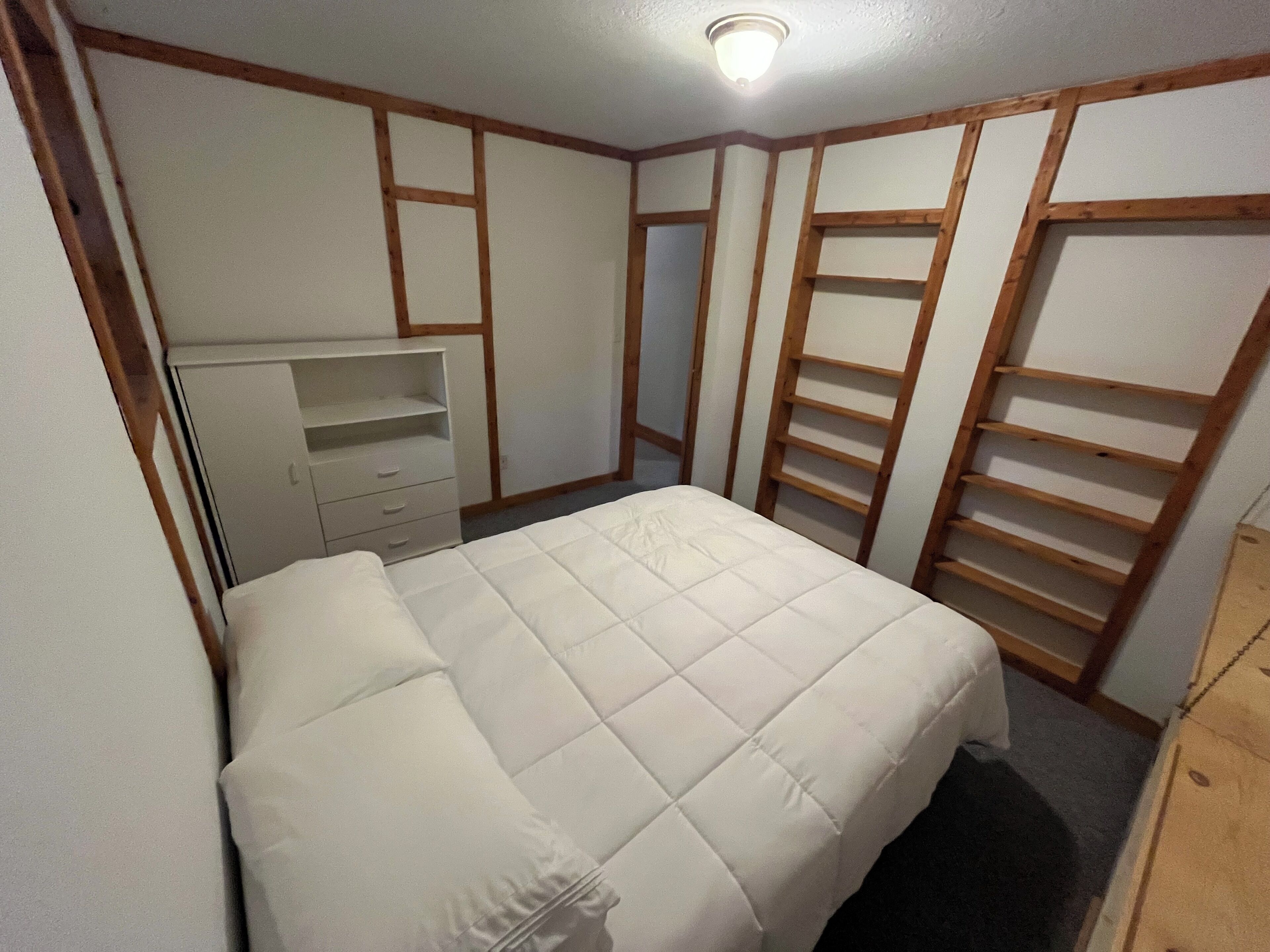 A bedroom with a bed, a dresser, a wardrobe, and built-in shelves.