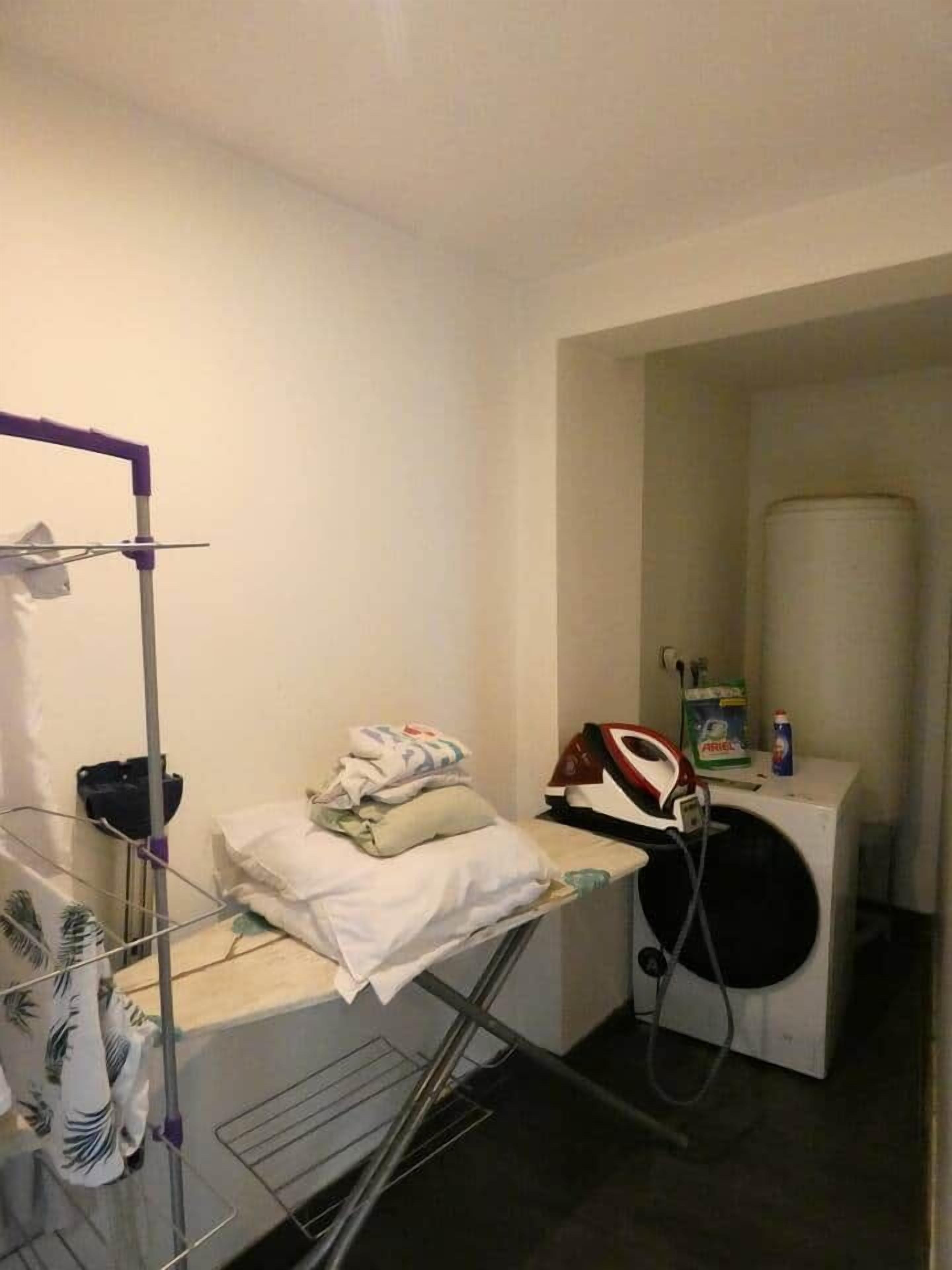 Ein kleiner Waschbereich mit Trockenständer, Bügeleisen und Waschmaschine.