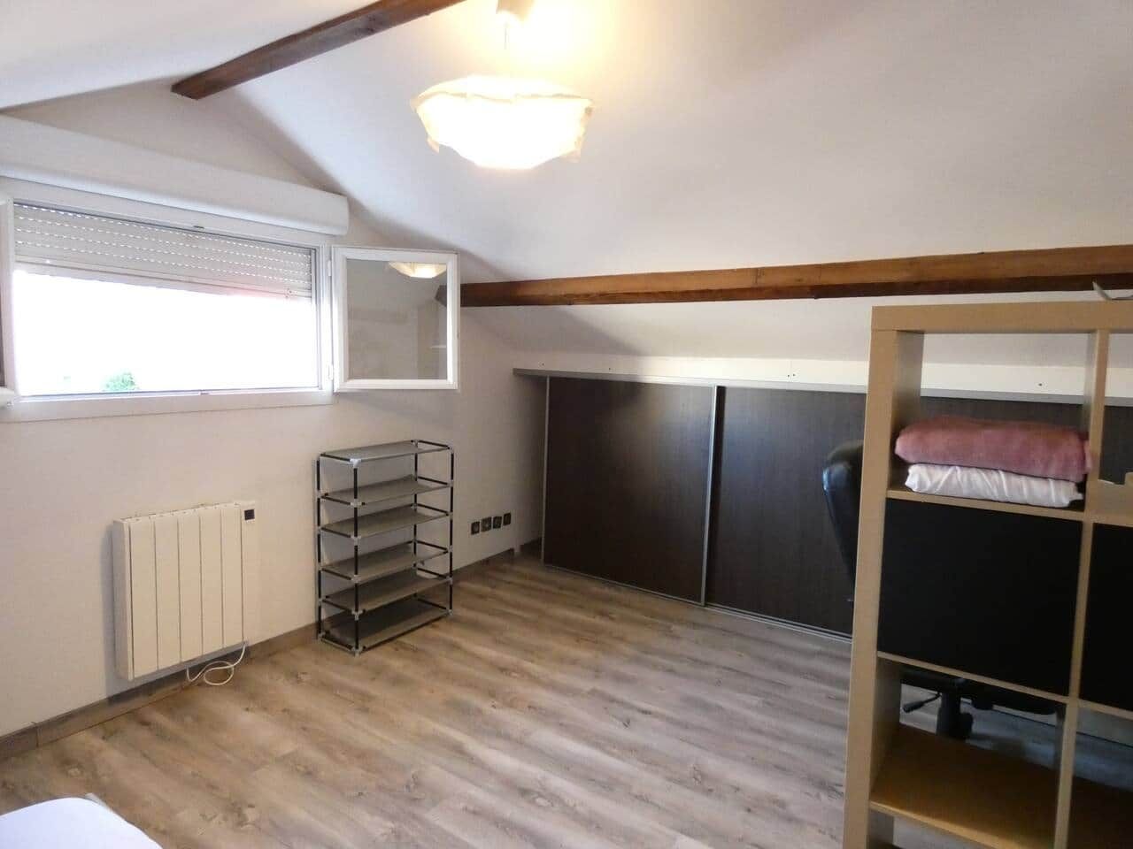 Une pièce avec un plafond en pente, un radiateur, une étagère en métal, un bureau avec une chaise et une armoire.