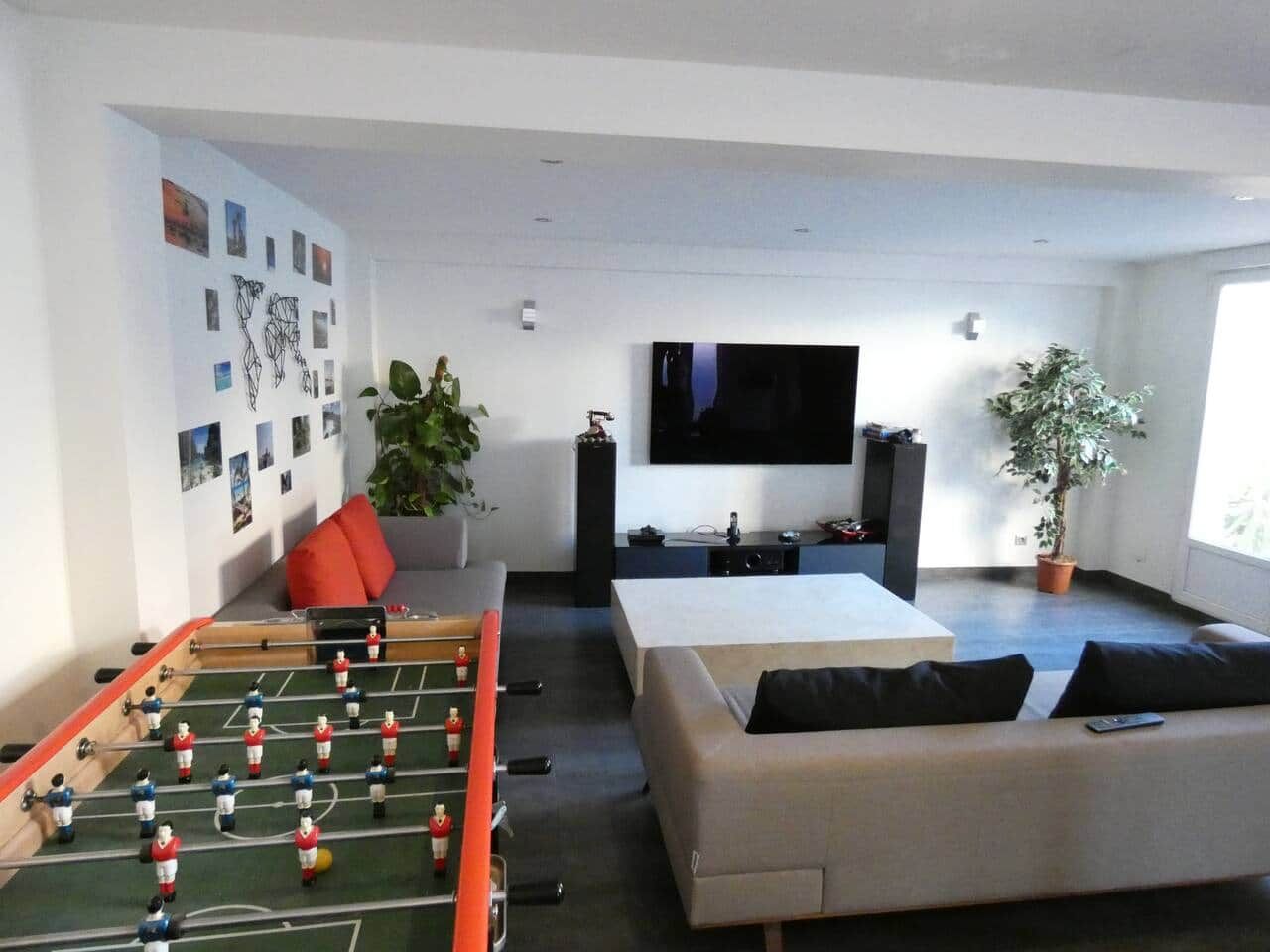 Ein modernes Wohnzimmer mit einem Kicker, einem großen Flachbildfernseher, einer Couch und einer Topfpflanze.