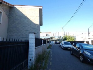 A narrow urban street with parked cars, a stone wall, and a metal fence. - Modern and spacious house with a swimming pool (Villeurbanne)