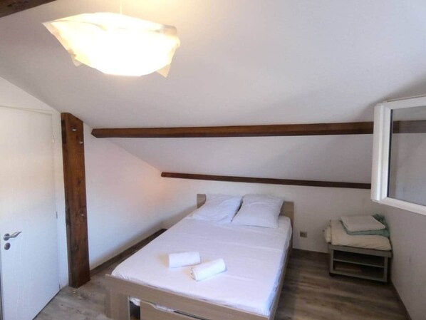 Une petite chambre avec un lit simple, une poutre en bois au plafond, une table de chevet et un téléviseur fixé au mur.