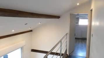 Ein modernes Interieur mit einer Holztreppe, einer Glastür, die nach draußen führt, und einem Flur mit Blick in einen weiteren Raum.