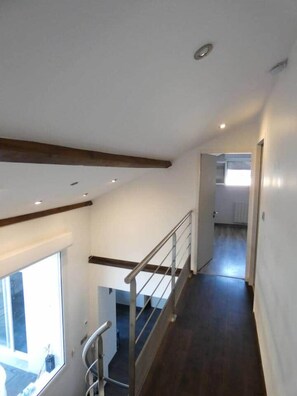 Un intérieur moderne avec un escalier en bois, une porte vitrée donnant sur l’extérieur et un couloir qui offre un aperçu d’une autre pièce.