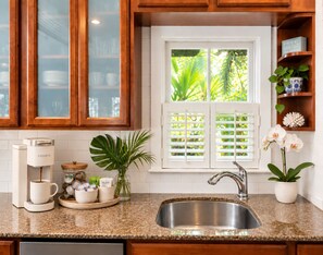 A kitchen with a coffee maker, a sink, and a window with shutters.