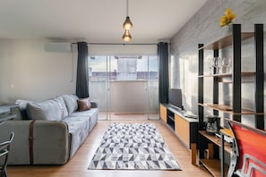 A modern living room with a grey sofa, a patterned rug, and a TV stand with a red chair.