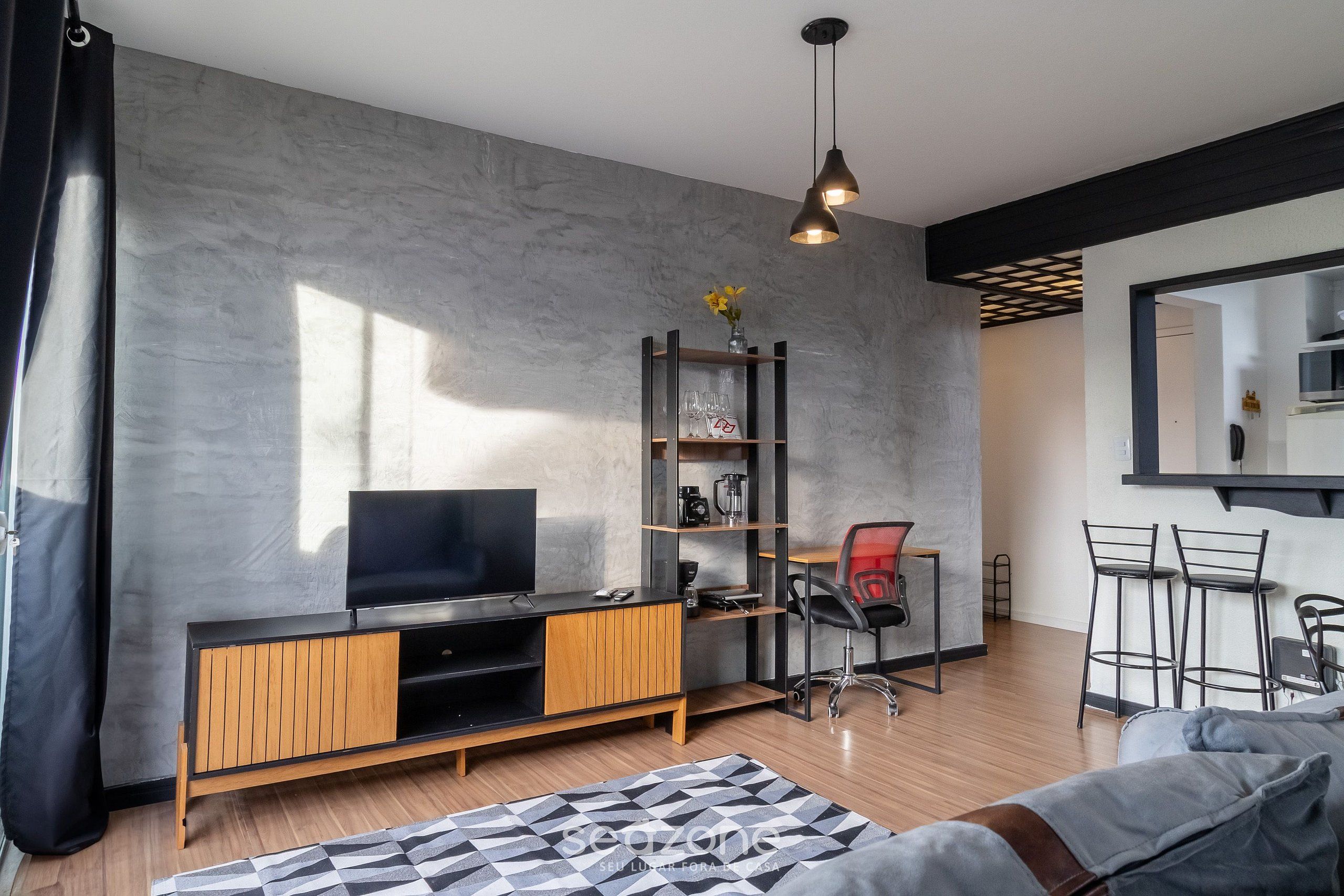 A modern living room with a TV, wooden entertainment unit, and a black office chair.