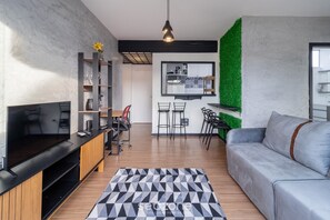 A modern living room with a flat-screen TV, wooden entertainment unit, and a grey sofa.