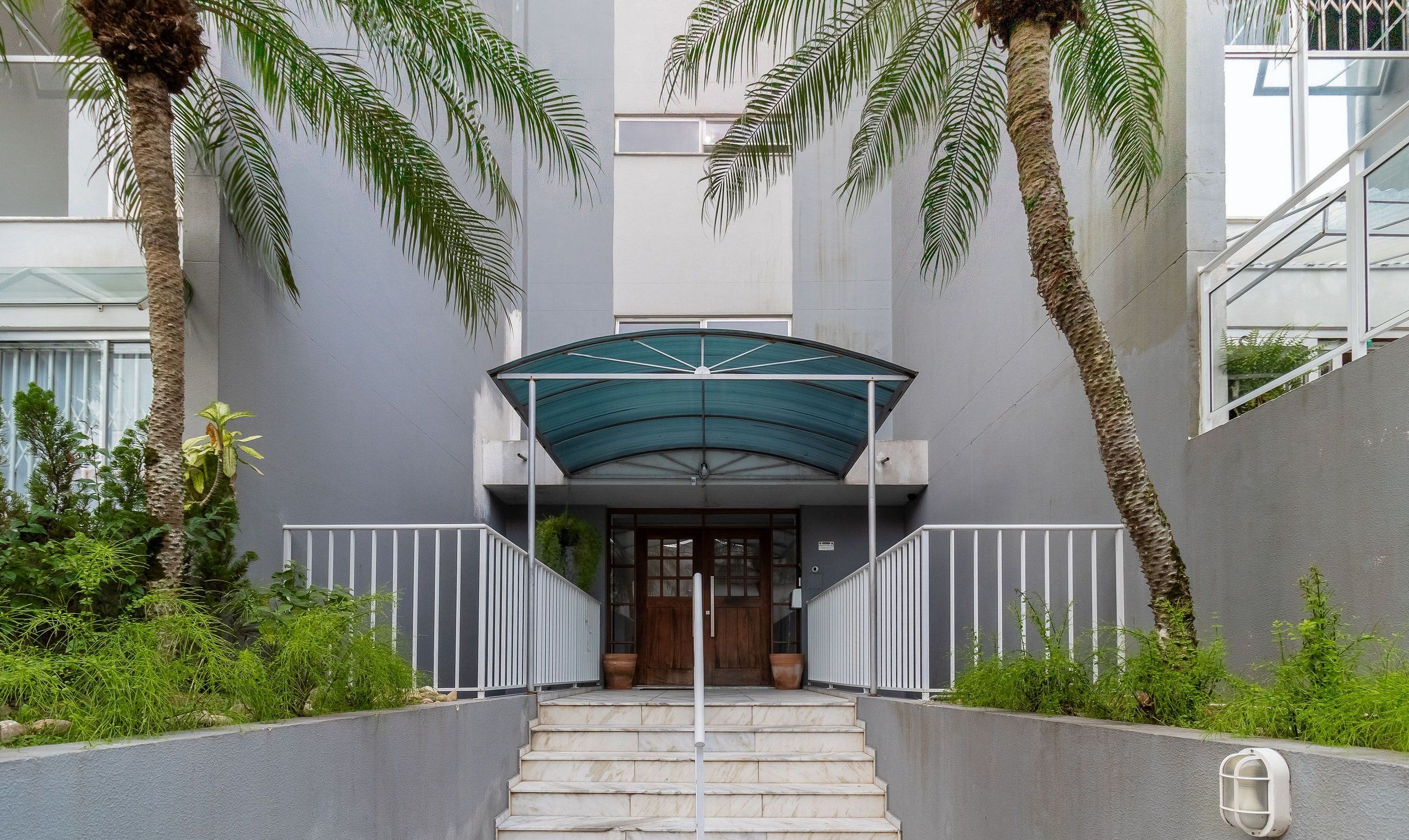 A building entrance with a covered entrance, steps leading up to it, and palm trees on either side.