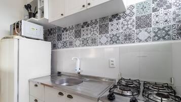 Una cocina compacta con lavamanos, estufa y gabinetes blancos.