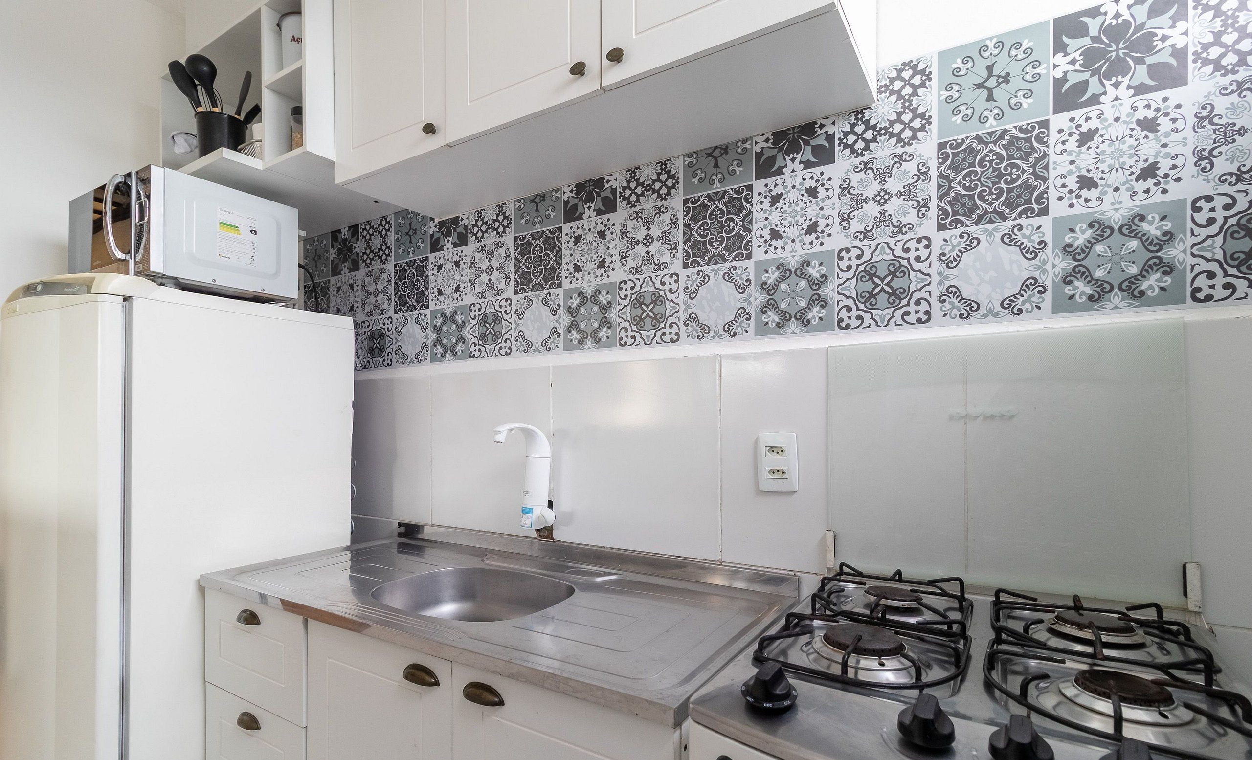 Una cocina compacta con lavamanos, estufa y gabinetes blancos.