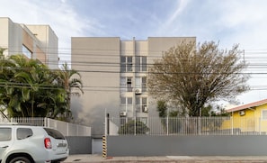 A modern building with a grey facade, a white fence, and a parked car.