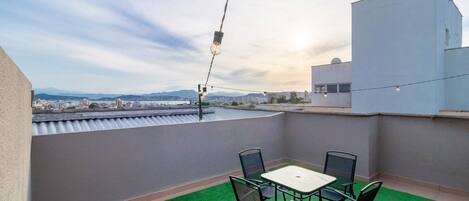 A rooftop terrace with a table and chairs, a hanging light fixture, and a view of the cityscape.