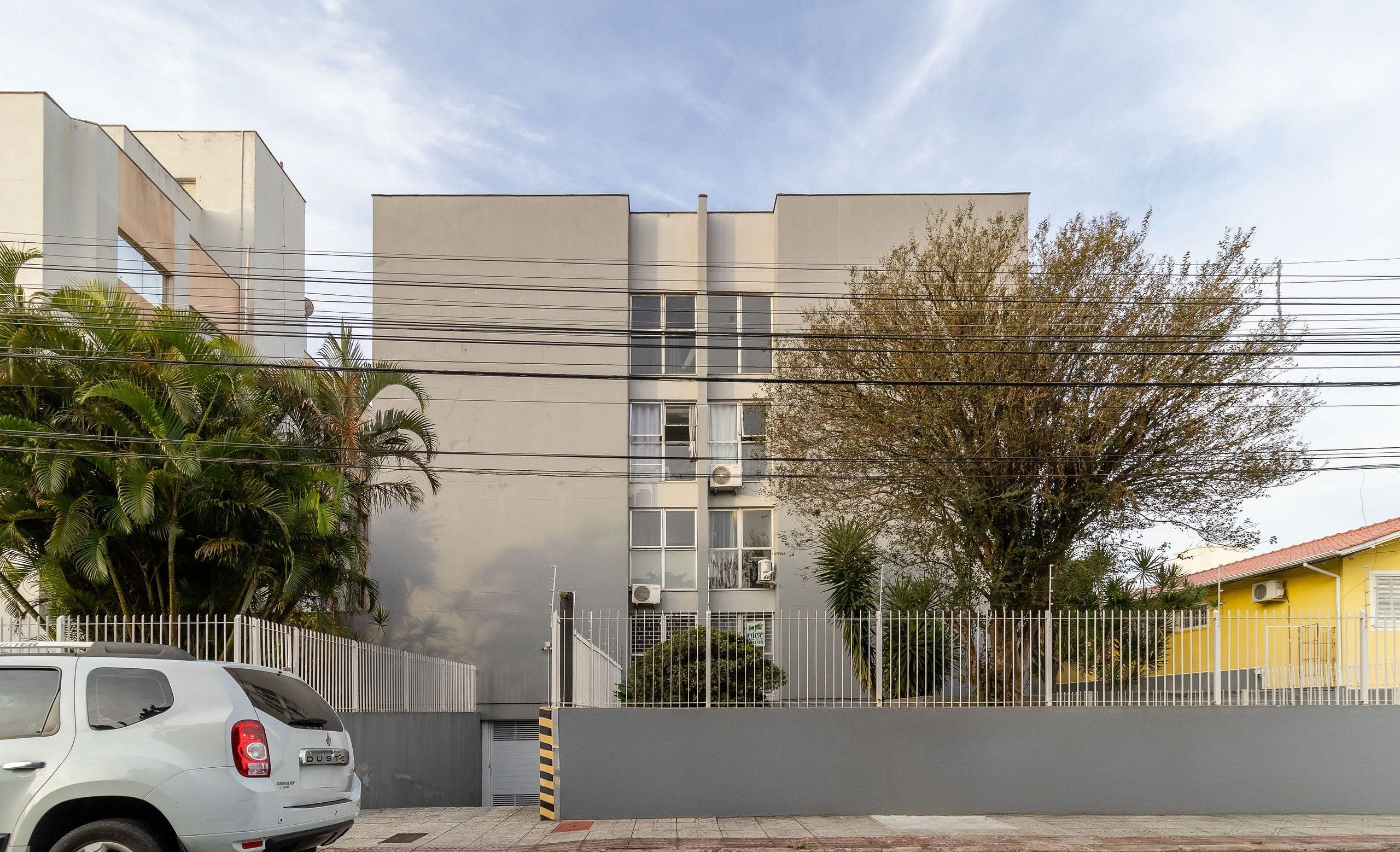 Un edificio moderno con fachada gris, una cerca blanca y un automóvil estacionado.