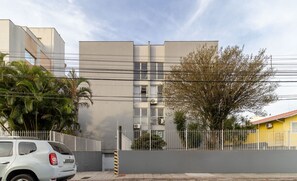 A modern building with a grey facade, a white fence, and a parked car.