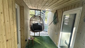 A wooden corridor with a hanging chair and a small table, leading to a glass door. - La Calypso de Paimpol (Paimpol)