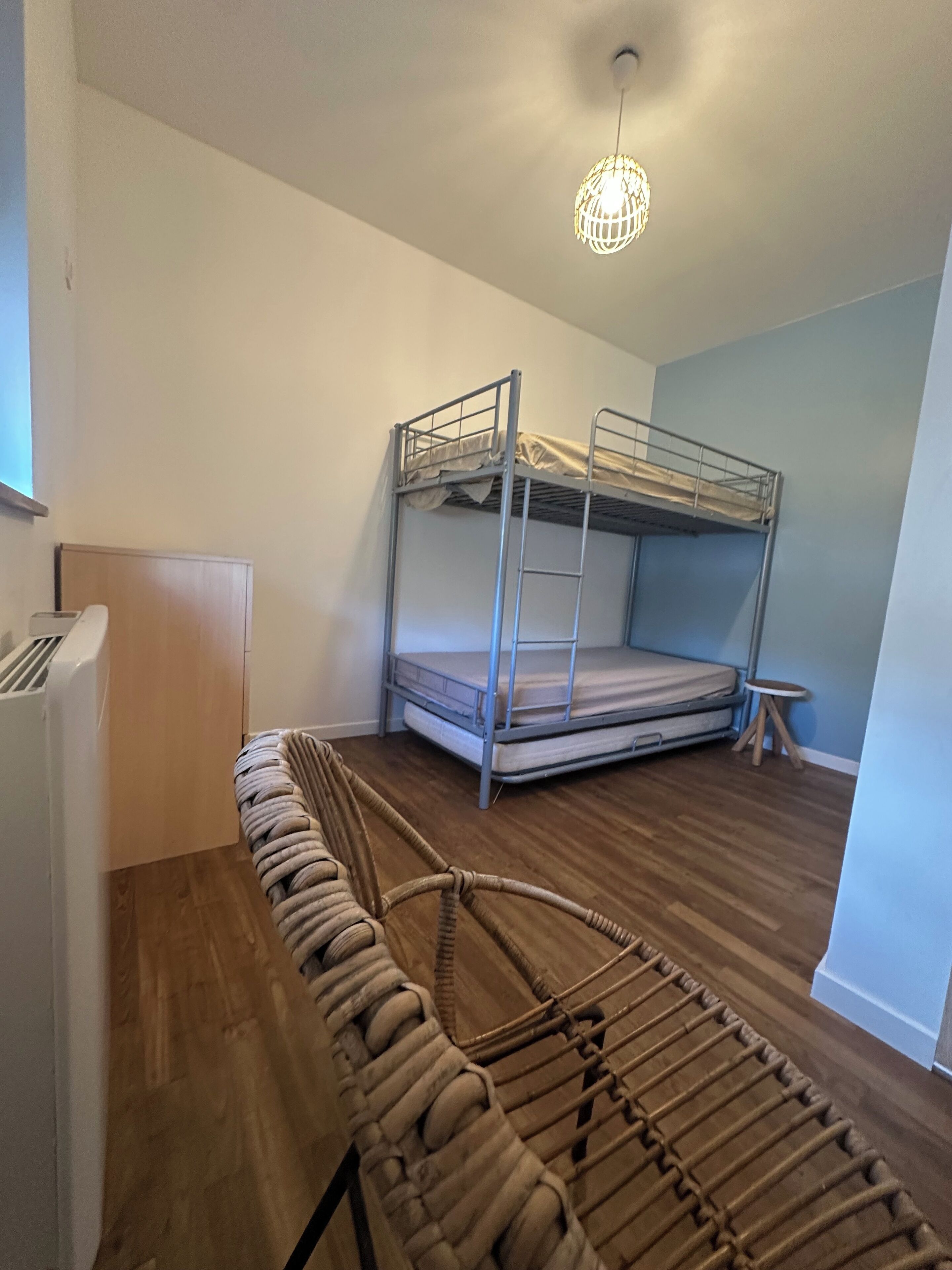 A bunk bed room with a hanging light fixture, a small stool, and a woven chair.