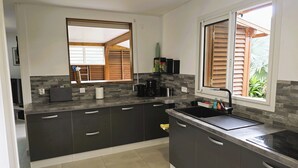 A modern kitchen with dark cabinets, a black countertop, and a window with wooden shutters. - Ti Kaz Romalex (Deshaies)