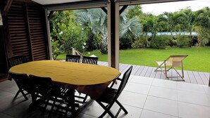 A covered patio with a wooden table and chairs, a tiled floor, and a view of a lush garden. - Ti Kaz Romalex (Deshaies)