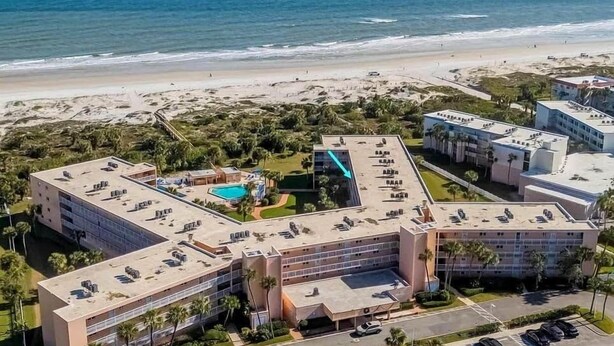 A resort with multiple buildings, a swimming pool, and a beach view.