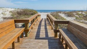 A wooden boardwalk leading to a beach with sandy dunes and a clear blue sky.