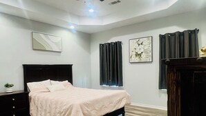 A bedroom with a bed, a ceiling fan, a nightstand, a dresser, and a window with curtains.