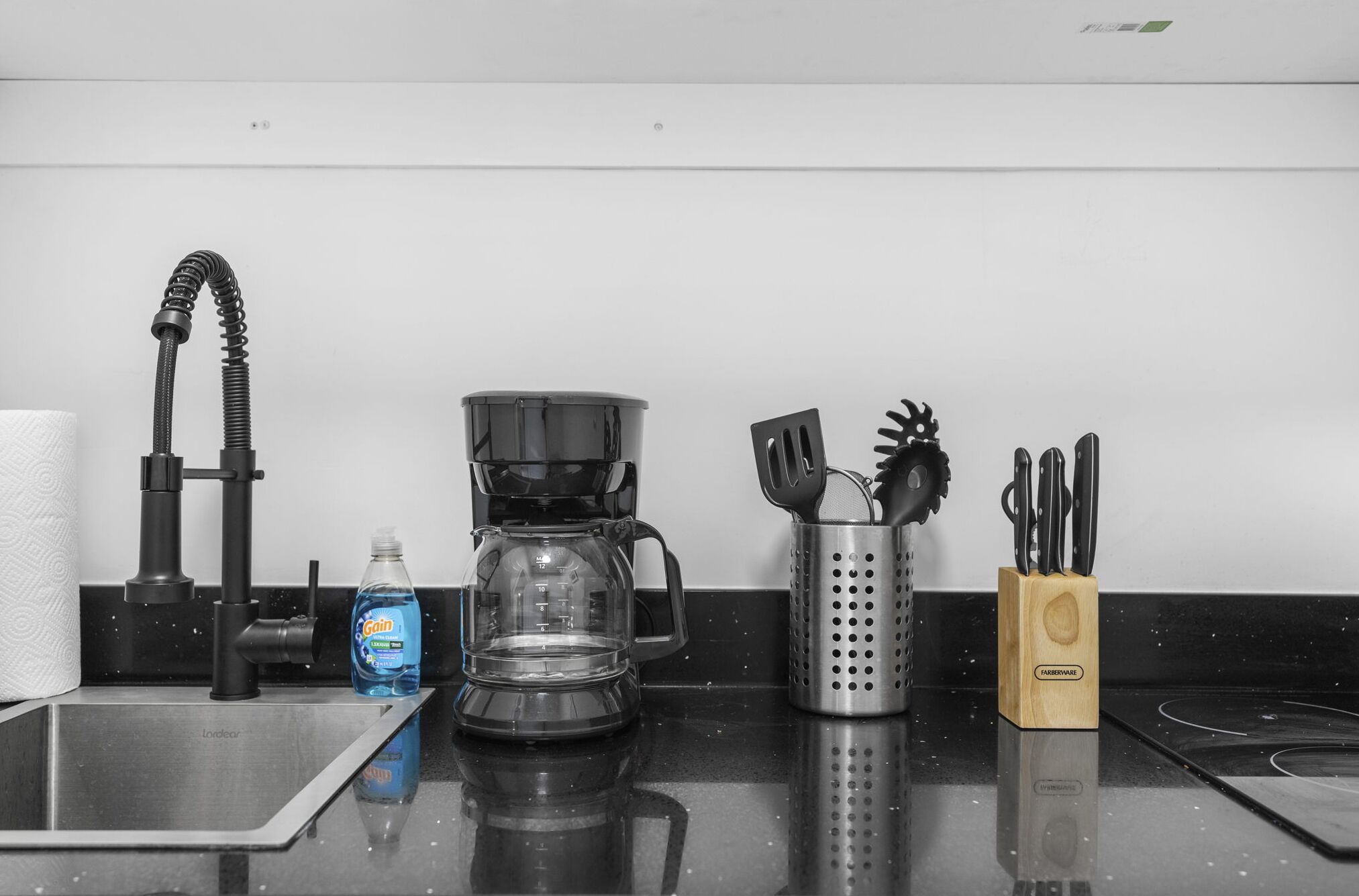 A kitchen with a coffee maker, a bottle of Gain dish soap, a colander, and a knife block.