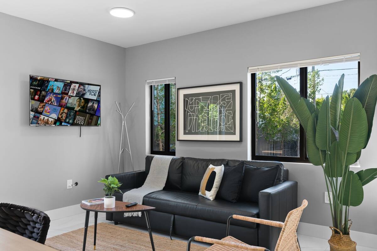 Un salon moderne avec un canapé en cuir noir, une table basse et une grande plante en pot.