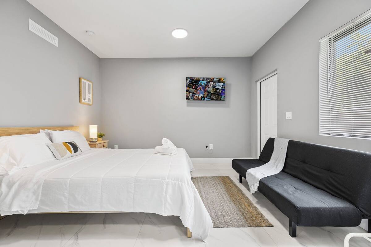 Une chambre moderne avec un grand lit, un canapé noir, une petite table avec une lampe et un tableau accroché au mur.