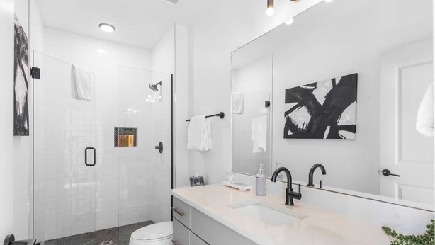 A modern bathroom with a glass shower enclosure, a white toilet, a sink with a mirror, and a towel rack. - Skyline Soundhouse by Avantstay Rooftop Deck & Game Room Near East Nashville & Broadway (Nashville)