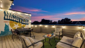 An outdoor patio with a seating area, a table with food, and a mural of Nashville. - Skyline Soundhouse by Avantstay Rooftop Deck & Game Room Near East Nashville & Broadway (Nashville)