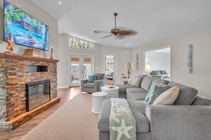 A spacious living room with a fireplace, comfortable seating, and a large TV screen displaying a tropical scene.