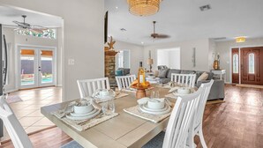 Un coin repas avec une table dressée pour six personnes, des chaises blanches et un lustre.