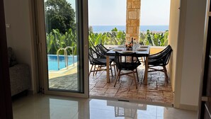 A spacious room with a large sliding glass door leading to an outdoor dining area with a view of the ocean.