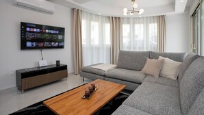 A modern living room with a grey sofa, a wooden coffee table, and a flat-screen TV mounted on the wall.