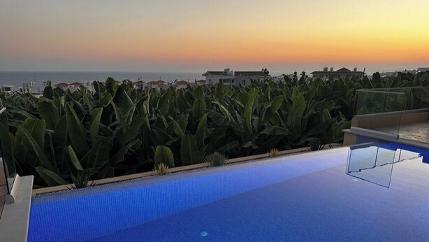 A rooftop infinity pool with a view of the sunset over the ocean.