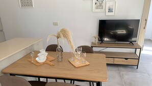 Een moderne eetruimte met een houten tafel, vier stoelen, een televisie en een vaas met pluimen.
