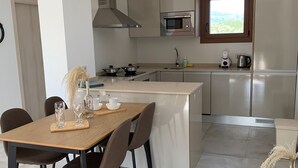 Een moderne keuken met een centraal eiland, een magnetron en een fornuis. Er is een eettafel met stoelen en een vaas met gedroogde bloemen.
